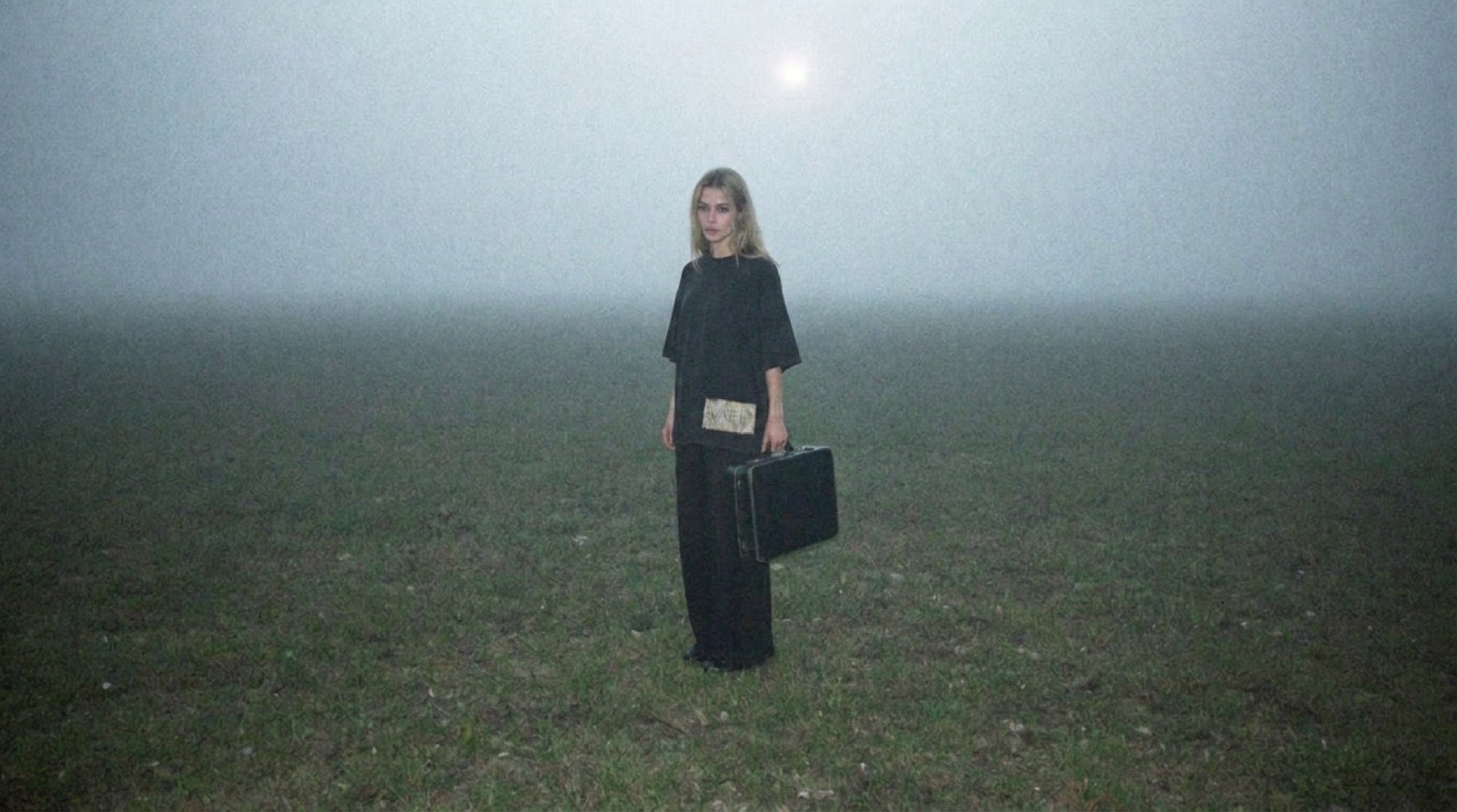 A figure in Garment 001 standing alone in a foggy field